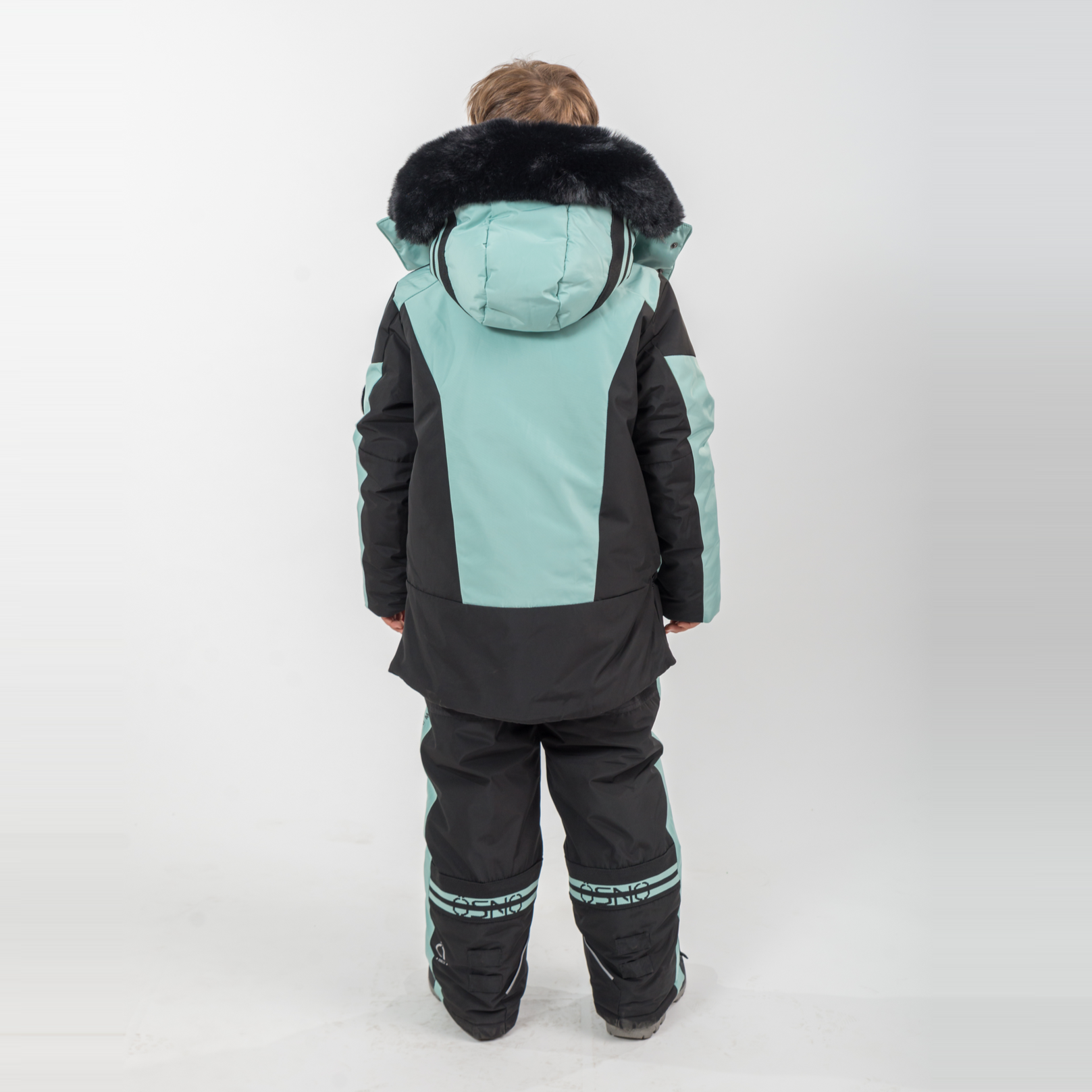 Child wearing a black and teal snowsuit with fur-lined hood on a white background