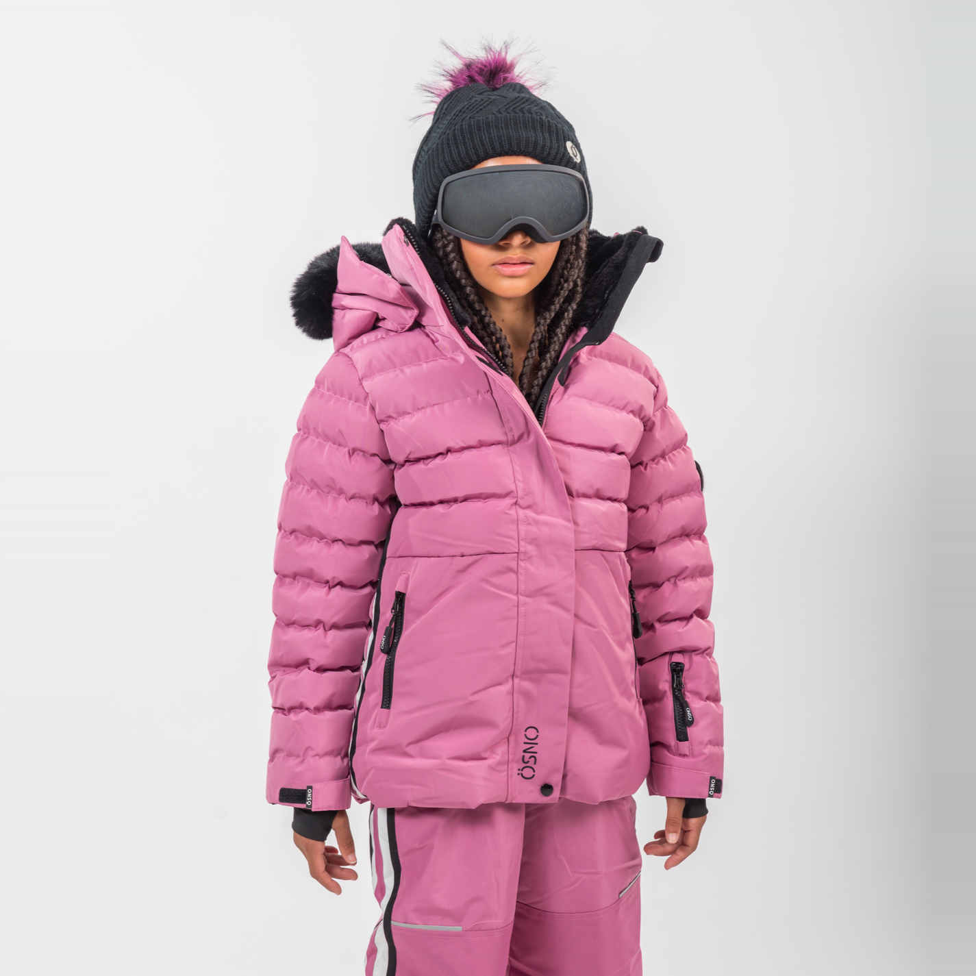 Person wearing a pink winter jacket and pants with goggles on a white background