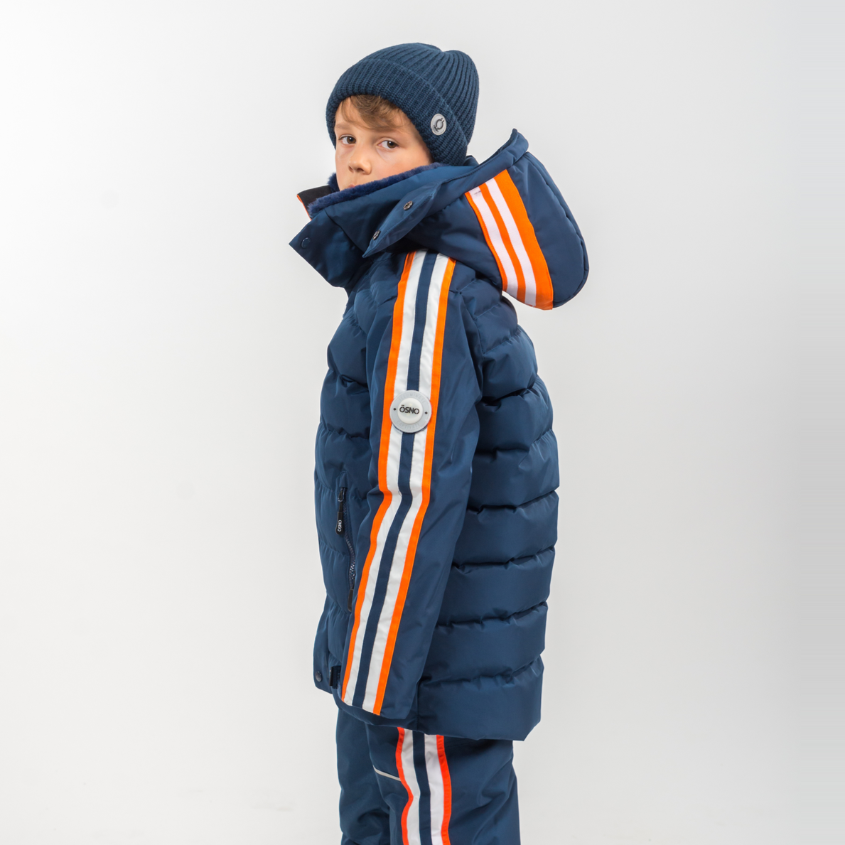 Child wearing a blue winter coat with orange and white stripes on a white background