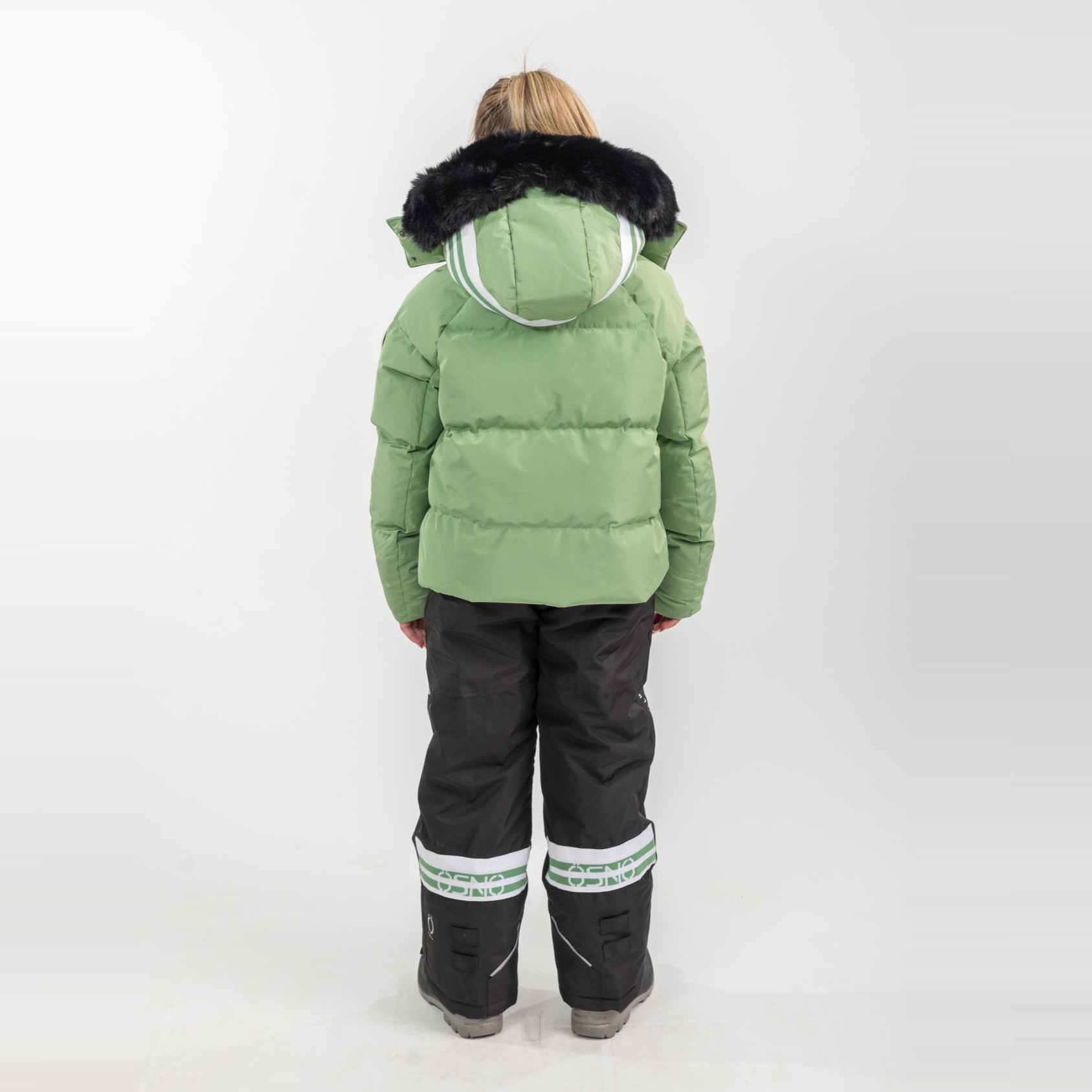 Person wearing a green winter jacket with fur hood and black pants on a white background