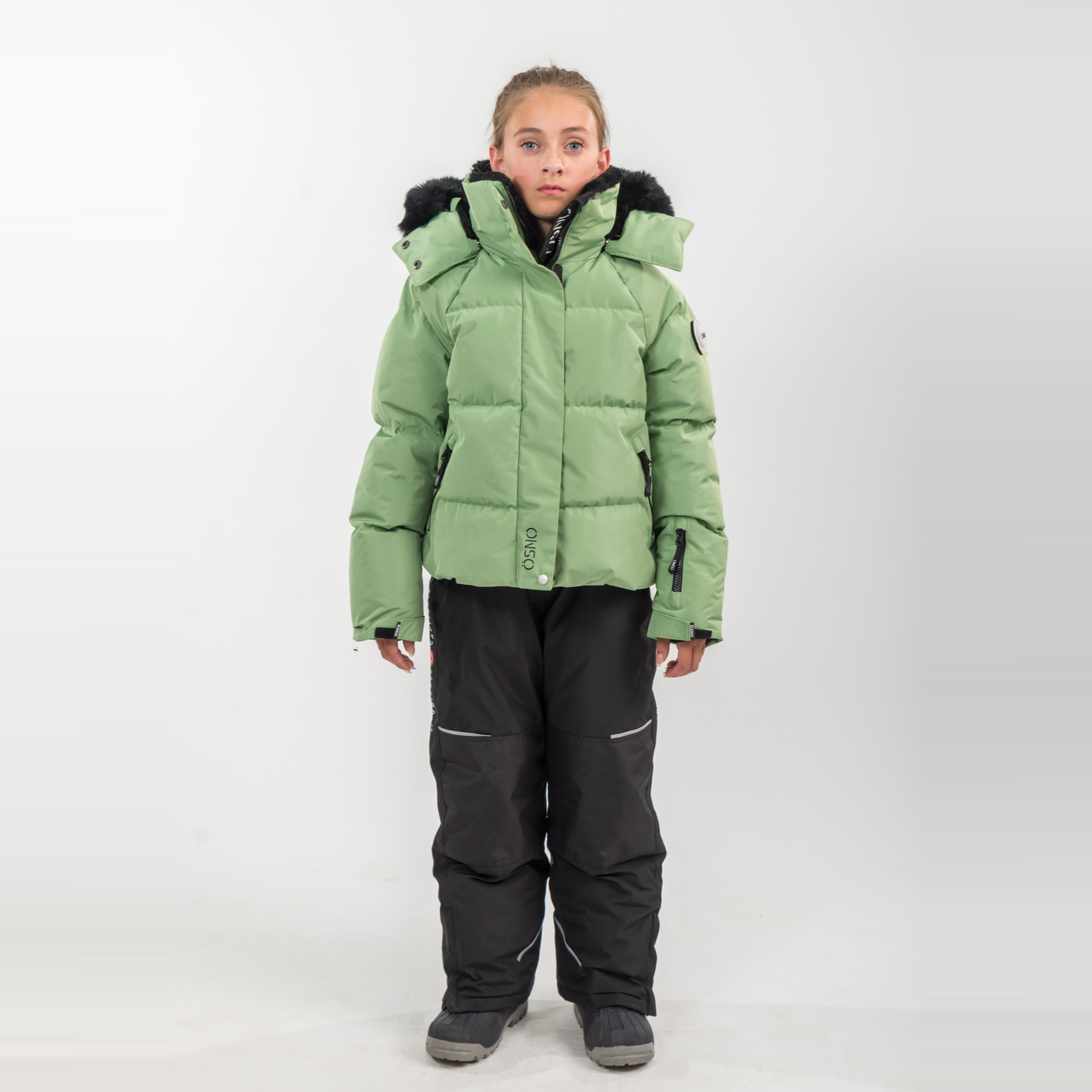 Person wearing a green puffer jacket and black pants on a white background